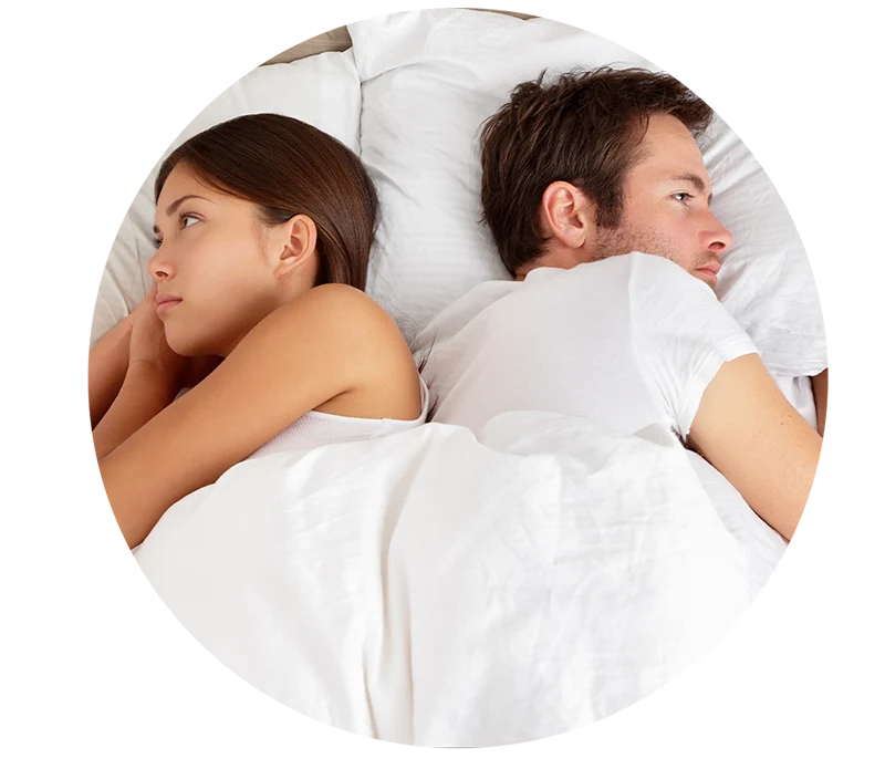 Upset young couple lying side by side in bed facing in opposite directions ignoring one another.